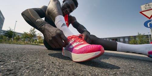 an athlete sat on the ground while lacing up his Adidas shoes an athlete sat on the ground while lacing up his Adidas shoes