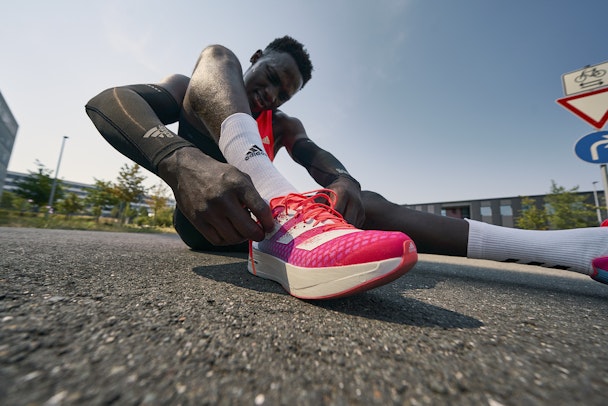 an athlete sat on the ground while lacing up his Adidas shoes