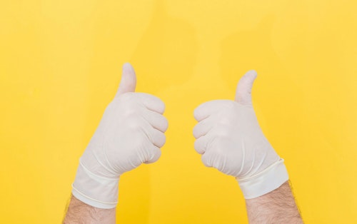 A pair of hands giving thumbs-up in surgical gloves