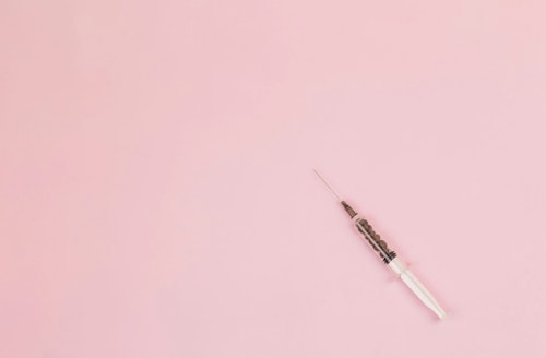 A syringe against a pink background