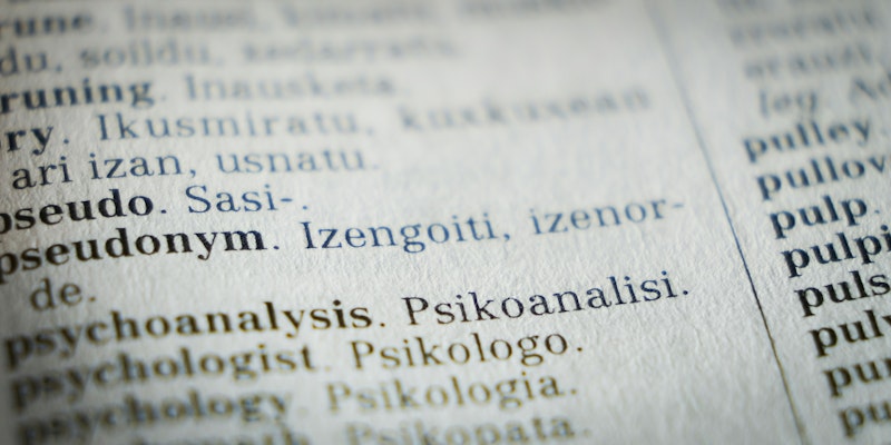 A close-up photograph of a page in the dictionary focuses on the word 'pseudonym'
