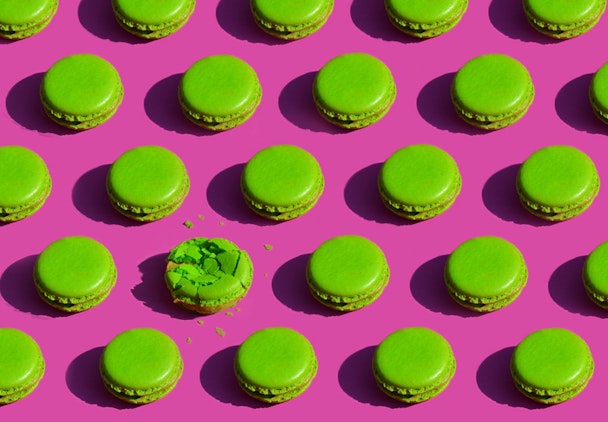 Green macarons on a pink background. One of them is smashed