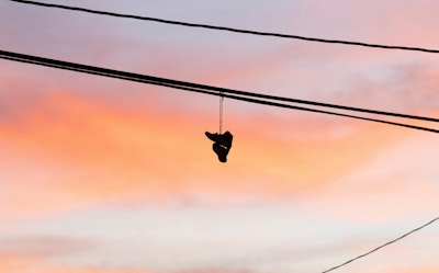 A pair of trainers or sneakers hangs over a telephone wire by the laces against a dawn or dusk sky