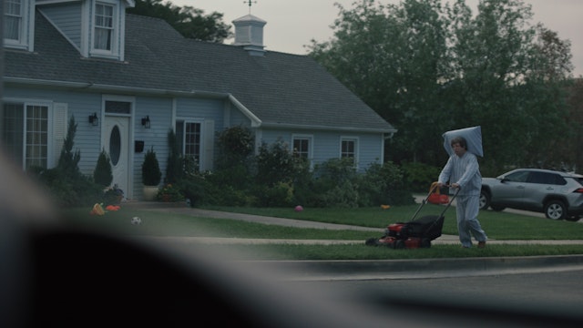 Man mowing lawn in pajamas with pillow stuck to his head