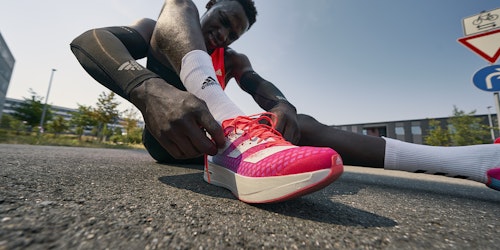 an athlete sat on the ground while lacing up his Adidas shoes