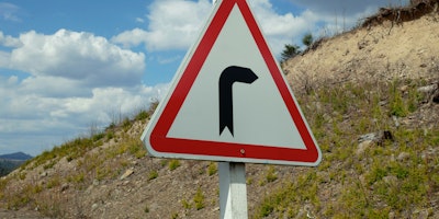 A white arrow with an angle bend in it is painted onto a grey paved raod 