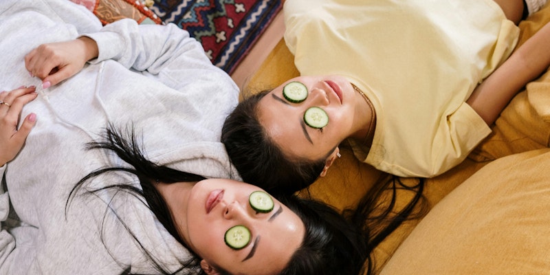 Two girls wearing cucumbers on their faces 