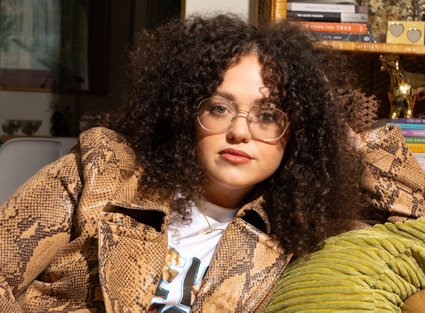 A woman with curly hair sitting on a couch wearing a green jacket