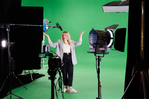 A woman standing in front of a green screen, with a digital camera in the foreground