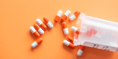 A pot of pills spilled over an orange surface