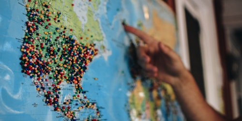 person pointing at a map of the world with pins on it