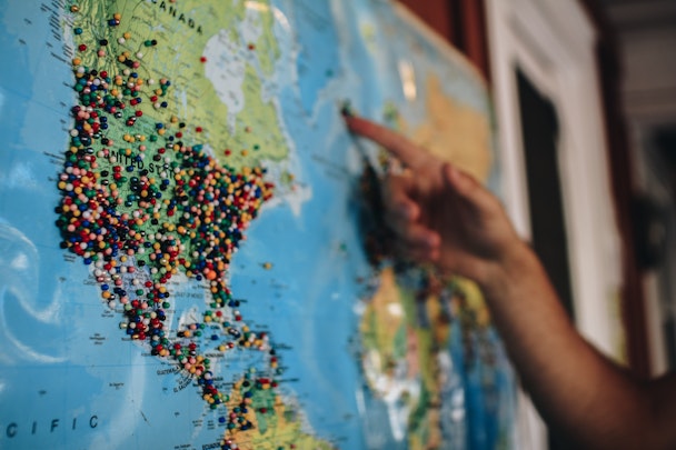 person pointing at a map of the world with pins on it