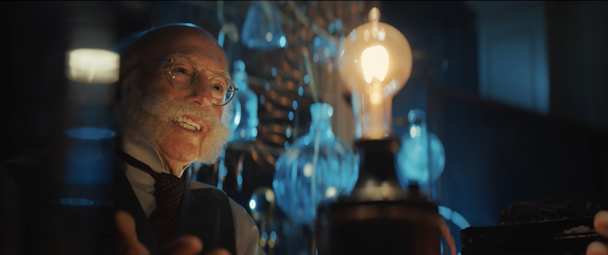 Larry David wearing a handlebar moustache, in front of an early lightbulb