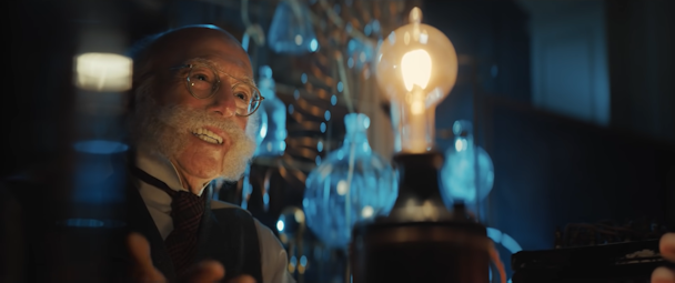 Larry David wearing a handlebar moustache, in front of an early lightbulb