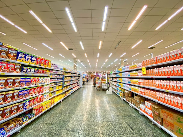 Supermarket aisles showing colourful goods on shelves, with a trolley in the distance