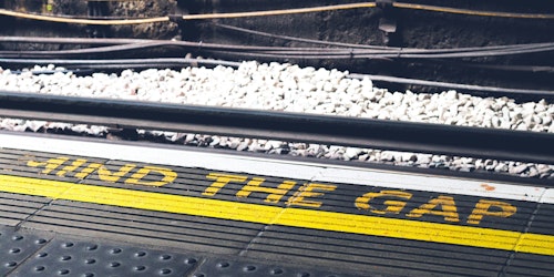 A photograph of a sign written on a London underground station platform reading 'mind the gap'