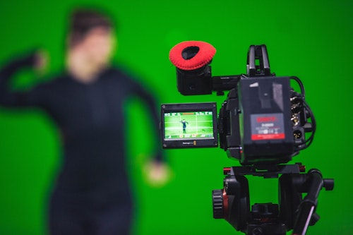 A camera in sharp focus, in front of a commercial green screen with trackers