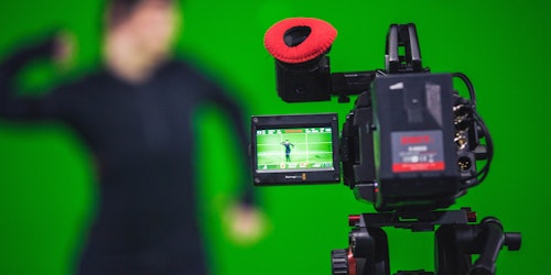 A camera in sharp focus, in front of a commercial green screen with trackers