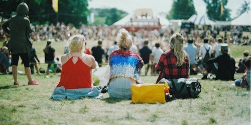 Three women sat on the ground at an outside event listening to musicians on the stage