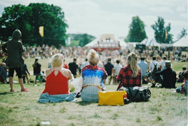 Three women sat on the ground at an outside event listening to musicians on the stage