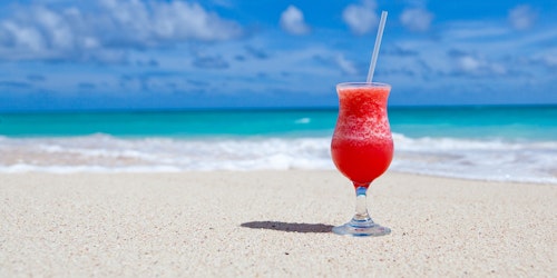 A tropical cocktail sitting on a beach under blue skies, with the ocean in the background