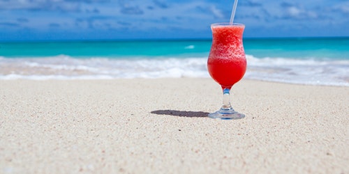 A tropical cocktail sitting on a beach under blue skies, with the ocean in the background