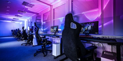 A bank of empty PCs of the sort used by esports professionals for training, lit in neon and purple