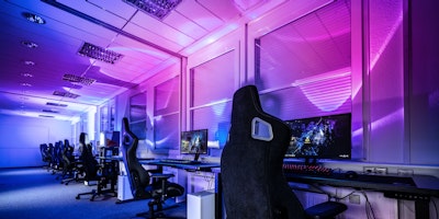 A bank of empty PCs of the sort used by esports professionals for training, lit in neon and purple