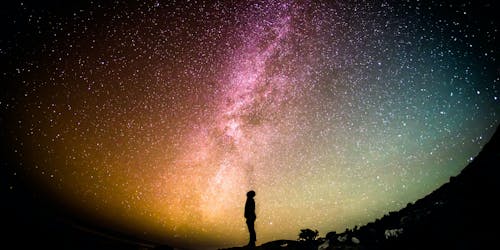 A man is silhouetted against a colourful nebula in a night's sky A man is silhouetted against a colourful nebula in a night's sky