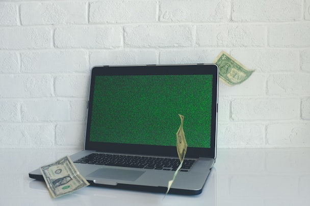 Dollar bills flutter in front of a blank screen, symbolising ad spend on fake sites