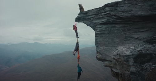 Three hikers dangling over the edge of a cliff using Macpac garments as ropes