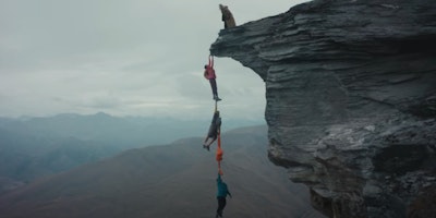 Three hikers dangling over the edge of a cliff using Macpac garments as ropes