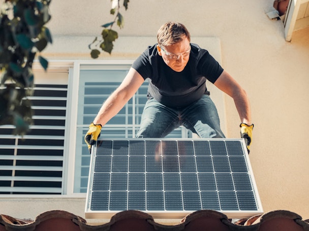 A man standing on a roof, fitting a solar panel