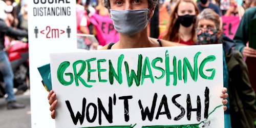a protestor holds a sign that says 'greenwashing won't wash'
