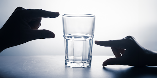 Glass with fingers showing half empty and half full