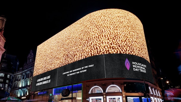 A large outdoor digital ad screen showing thousands of candles being lit