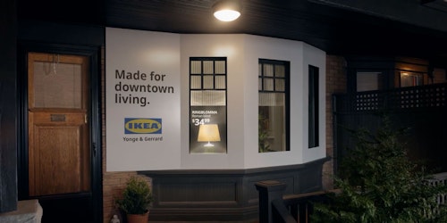 The porch of a house, the bay window of which has been turned into a billboard ad for Ikea with product name and price of the lamp visable inside written on the window