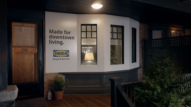 The porch of a house, the bay window of which has been turned into a billboard ad for Ikea with product name and price of the lamp visable inside written on the window