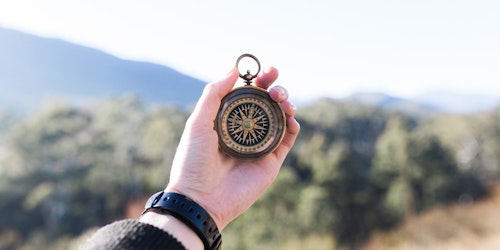 Photograph of a hand holding a compass in front of a blurred landscape