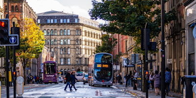 Photograph of Princess Street, Manchester showing people crossing the road and buses in front of buildings