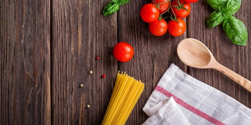 Photograph of tomatoes, basil and uncooked spaghetti on a wooden worktop