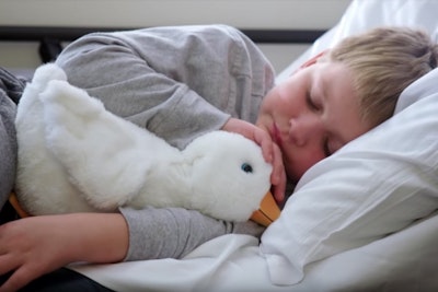 A young boy in bed cuddling a toy duck.