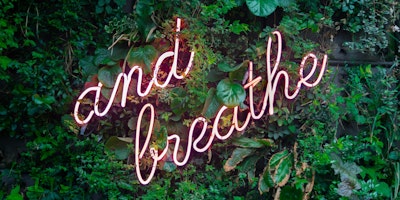 A neon wall-mounted sign reading: "And Breathe..."