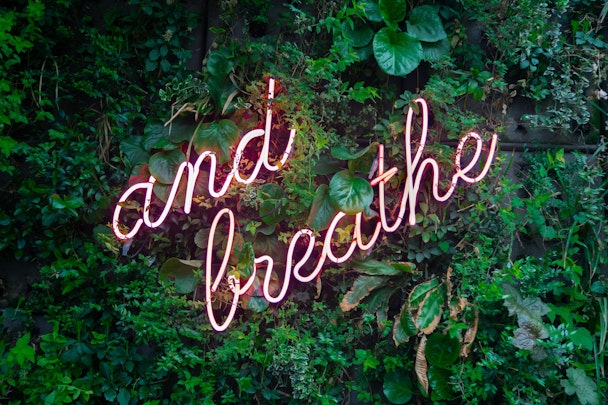 A neon wall-mounted sign reading: "And Breathe..."