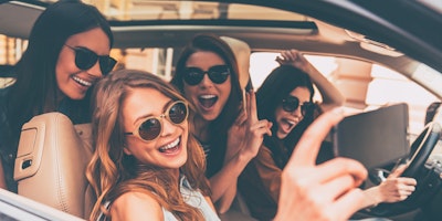 Four young women chat happily inside a car on a summer trip.