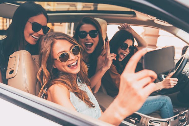 Four young women chat happily inside a car on a summer trip. Four young women chat happily inside a car on a summer trip.