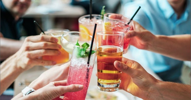 Five hands hold colourful drinks together to say "Cheers!"