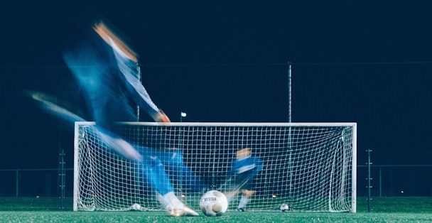 A blurred player hits a penalty against a goalkeeper.
