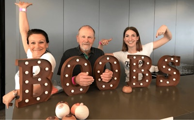 Three Mando team members sit behind large letters spelling the word 'boobs'.