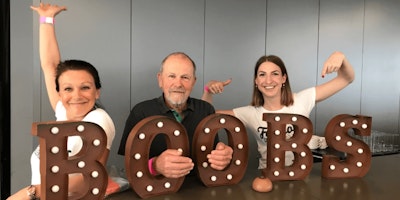 Three Mando team members sit behind large letters spelling the word 'boobs'.